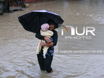 A Nepali woman carries a baby and wades through floodwater in Kathmandu, Nepal, on September 27, 2024. The Himalayan nation witnesses downpo...