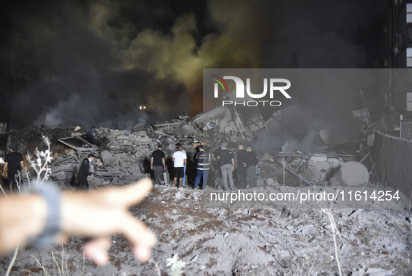 People watch as a blaze rages amid the smoldering rubble of a building destroyed in an Israeli air strike in the Haret Hreik neighborhood of...