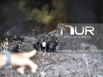 People watch as a blaze rages amid the smoldering rubble of a building destroyed in an Israeli air strike in the Haret Hreik neighborhood of...