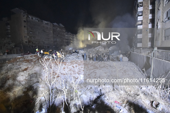 People watch as a blaze rages amid the smoldering rubble of a building destroyed in an Israeli air strike in the Haret Hreik neighborhood of...