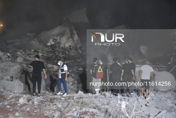 People watch as a blaze rages amid the smoldering rubble of a building destroyed in an Israeli air strike in the Haret Hreik neighborhood of...