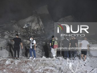 People watch as a blaze rages amid the smoldering rubble of a building destroyed in an Israeli air strike in the Haret Hreik neighborhood of...