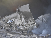 People watch as a blaze rages amid the smoldering rubble of a building destroyed in an Israeli air strike in the Haret Hreik neighborhood of...