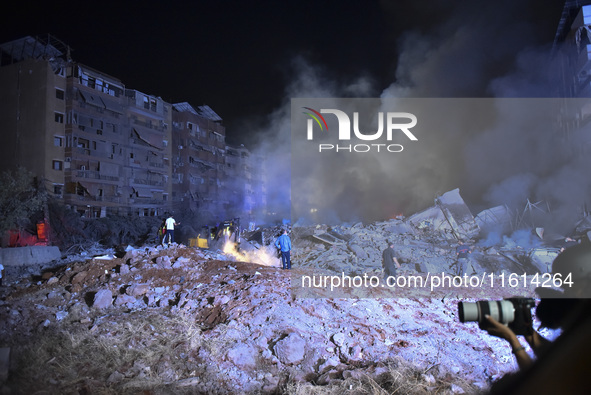 People watch as a blaze rages amid the smoldering rubble of a building destroyed in an Israeli air strike in the Haret Hreik neighborhood of...