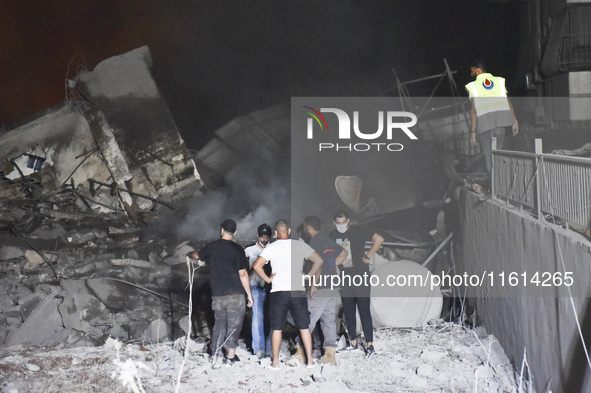 People watch as a blaze rages amid the smoldering rubble of a building destroyed in an Israeli air strike in the Haret Hreik neighborhood of...