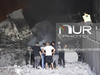 People watch as a blaze rages amid the smoldering rubble of a building destroyed in an Israeli air strike in the Haret Hreik neighborhood of...