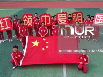 Students pose for a photo with the national flag at the Jindu Huating campus of Xiaoyaojin Primary School in Hefei, China, on September 27,...