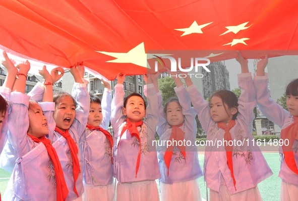 Students pose for a photo with the national flag at the Jindu Huating campus of Xiaoyaojin Primary School in Hefei, China, on September 27,...