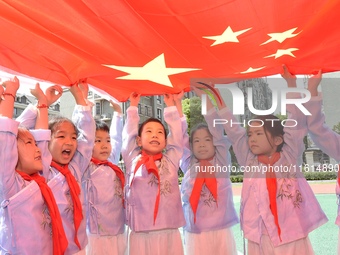 Students pose for a photo with the national flag at the Jindu Huating campus of Xiaoyaojin Primary School in Hefei, China, on September 27,...