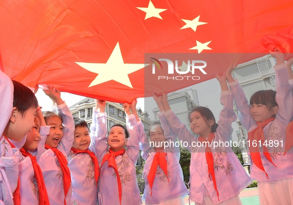 Students pose for a photo with the national flag at the Jindu Huating campus of Xiaoyaojin Primary School in Hefei, China, on September 27,...