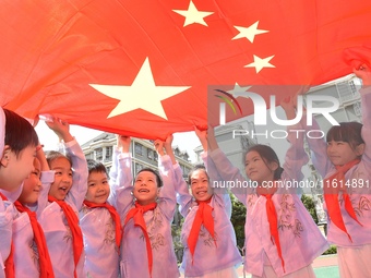 Students pose for a photo with the national flag at the Jindu Huating campus of Xiaoyaojin Primary School in Hefei, China, on September 27,...