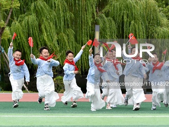 Students run on the playground with a small national flag at the Jindu Huating campus of Xiaoyaojin Primary School in Hefei, China, on Septe...