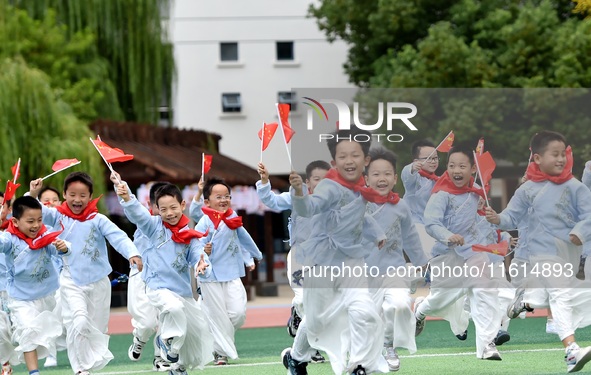 Students run on the playground with a small national flag at the Jindu Huating campus of Xiaoyaojin Primary School in Hefei, China, on Septe...