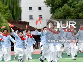 Students run on the playground with a small national flag at the Jindu Huating campus of Xiaoyaojin Primary School in Hefei, China, on Septe...