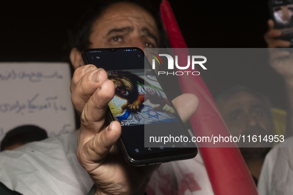 An Iranian protester holds his cellphone featuring an anti-Israeli illustration during a protest gathering to condemn an Israeli air strike...