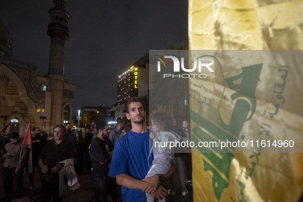 An Iranian protester holds his child while standing next to a flag of Lebanon's Hezbollah during a protest gathering to condemn an Israeli a...