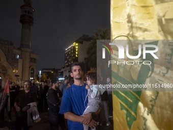 An Iranian protester holds his child while standing next to a flag of Lebanon's Hezbollah during a protest gathering to condemn an Israeli a...