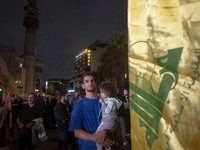 An Iranian protester holds his child while standing next to a flag of Lebanon's Hezbollah during a protest gathering to condemn an Israeli a...