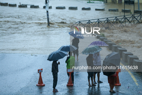 Residents of Kathmandu stand on the embankment of a flooded river in Kathmandu, Nepal, on September 28, 2024, after an overnight heavy downp...