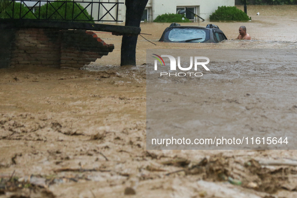 A man wades through the flooded river to reach his partially submerged car in Lalitpur, Nepal, on September 28, 2024. At least 32 people die...