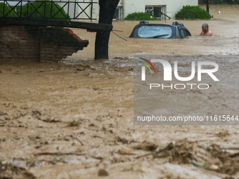 A man wades through the flooded river to reach his partially submerged car in Lalitpur, Nepal, on September 28, 2024. At least 32 people die...