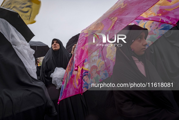 A young veiled Iranian girl holds an umbrella printed with images of Disney characters while participating in a protest gathering with her m...