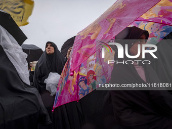 A young veiled Iranian girl holds an umbrella printed with images of Disney characters while participating in a protest gathering with her m...