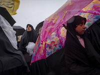 A young veiled Iranian girl holds an umbrella printed with images of Disney characters while participating in a protest gathering with her m...