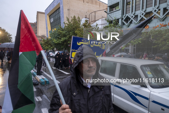 An Iranian protester holds a Palestinian flag while standing next to a vehicle carrying a scaled model of Iran's first ultrasonic missile (F...