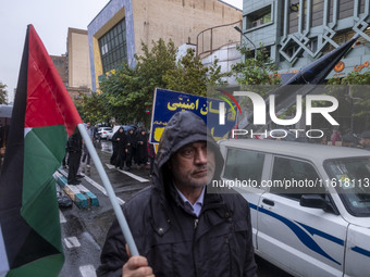 An Iranian protester holds a Palestinian flag while standing next to a vehicle carrying a scaled model of Iran's first ultrasonic missile (F...