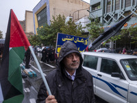 An Iranian protester holds a Palestinian flag while standing next to a vehicle carrying a scaled model of Iran's first ultrasonic missile (F...