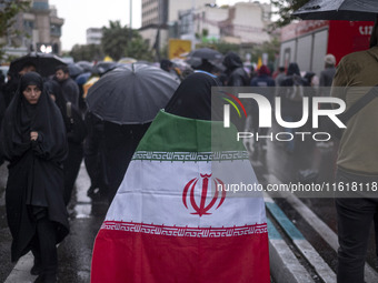 A veiled Iranian protester wears an Iranian flag while taking part in a protest gathering to condemn an Israeli air strike against Hezbollah...