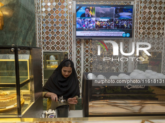 An Iranian female barista works at a cafe, while a portrait of Lebanon's Hezbollah Secretary General, Hassan Nasrallah, who was killed in an...