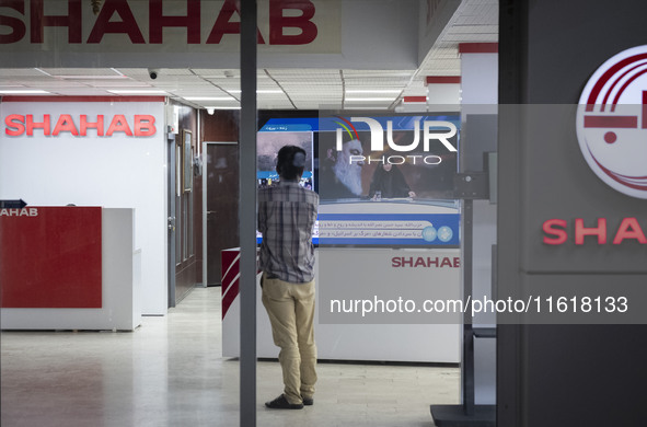 An Iranian employee looks at a television featuring a portrait of Lebanon's Hezbollah Secretary General, Hassan Nasrallah, who was killed in...