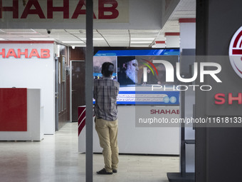 An Iranian employee looks at a television featuring a portrait of Lebanon's Hezbollah Secretary General, Hassan Nasrallah, who was killed in...