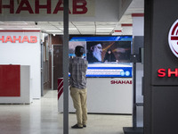 An Iranian employee looks at a television featuring a portrait of Lebanon's Hezbollah Secretary General, Hassan Nasrallah, who was killed in...