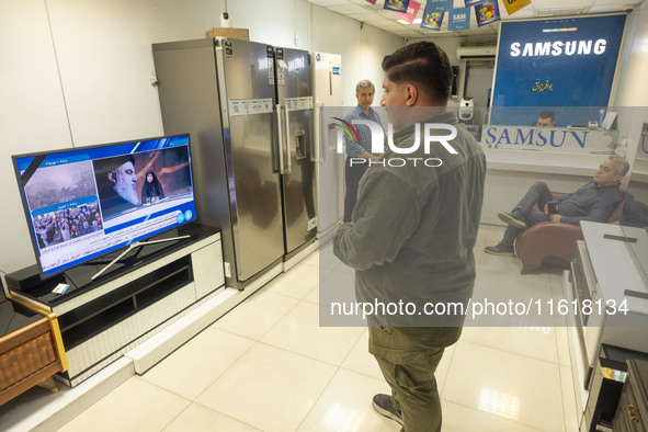 Iranian traders look at a television featuring a portrait of Lebanon's Hezbollah Secretary General, Hassan Nasrallah, who was killed in an I...