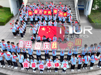 Primary school students pose for a photo with the national flag to celebrate the 75th anniversary of the founding of China in Taicang, Jiang...