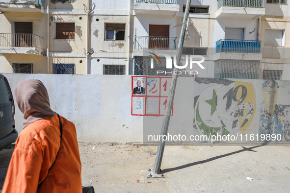 A woman walks past an election poster of presidential candidate Kais Saied stuck on a wall along a street in Ariana, Tunisia, on September 2...