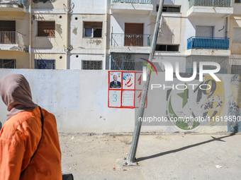 A woman walks past an election poster of presidential candidate Kais Saied stuck on a wall along a street in Ariana, Tunisia, on September 2...