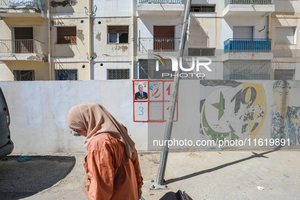 A woman walks past an election poster of presidential candidate Kais Saied stuck on a wall along a street in Ariana, Tunisia, on September 2...