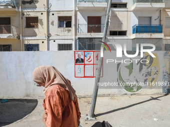 A woman walks past an election poster of presidential candidate Kais Saied stuck on a wall along a street in Ariana, Tunisia, on September 2...