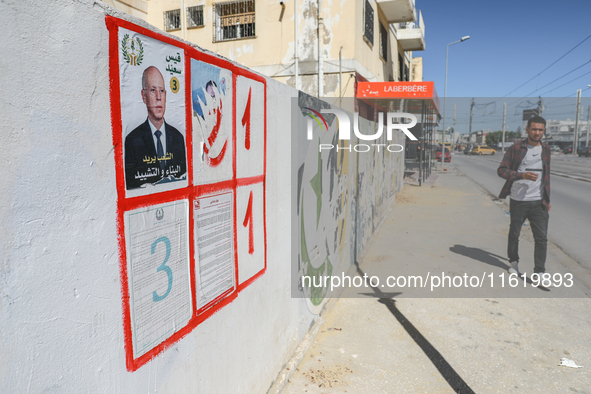 A young man walks past an election poster of presidential candidate Kais Saied stuck on a wall along a street in Ariana, Tunisia, on Septemb...