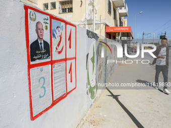 A young man walks past an election poster of presidential candidate Kais Saied stuck on a wall along a street in Ariana, Tunisia, on Septemb...