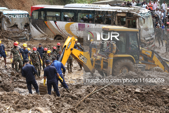 Excavators comb through the mud in search of bodies of passengers believed to be buried in the landslide that covers multiple vehicles at Jh...