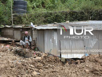 A Nepali man rests next to a tin shelter damaged by a landslide in Dhading district of Central Nepal on September 29, 2024. At least 35 peop...