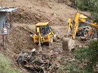 Excavators comb through the mud in search of bodies of passengers believed to be buried in the landslide that covers multiple vehicles at Jh...