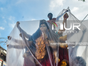 Laborers cover a Durga idol with plastic to protect it from rain on a truck for transport to a pandal, or a temporary platform, ahead of the...