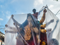 Laborers cover a Durga idol with plastic to protect it from rain on a truck for transport to a pandal, or a temporary platform, ahead of the...