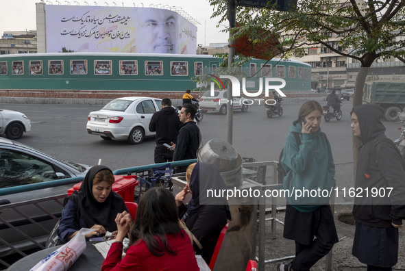 A group of young Iranian women, some of whom are not wearing mandatory headscarves, sit and stand at an outdoor fast-food restaurant in down...